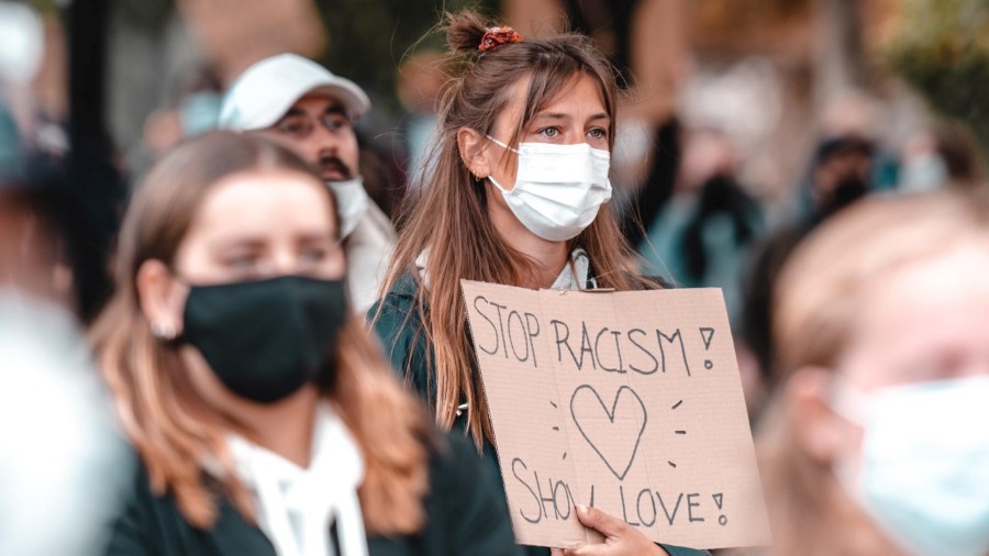 junge Demonstrantin mit Maske hält "Stop Racism, show love"-Schild